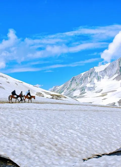 Horse riders crossing a snowfield below mountain peaks in Kashmir
